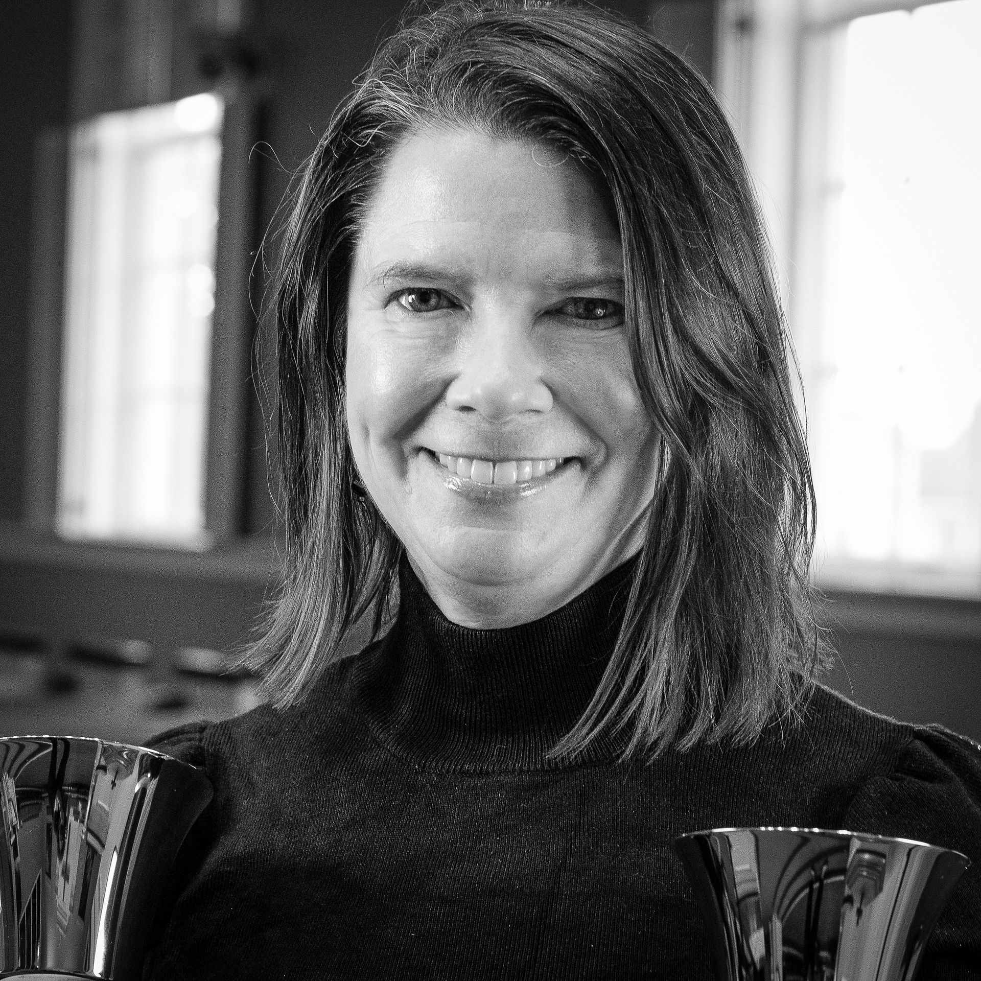 Woman with dark hair smiles, holding handbells, indoors.