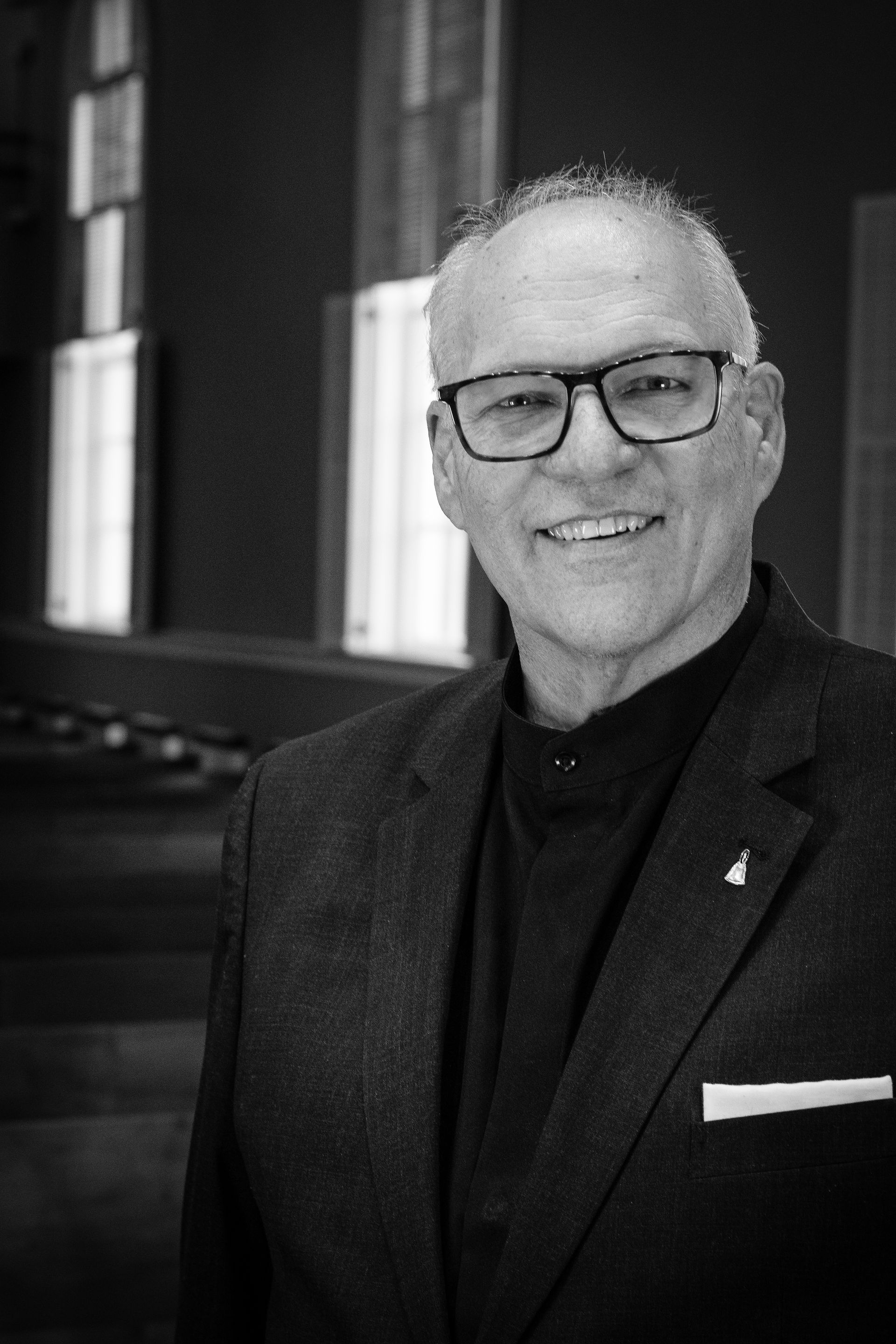 Man with glasses smiling in a dark suit. Artistic director for Lancaster Handbell Ensemble.