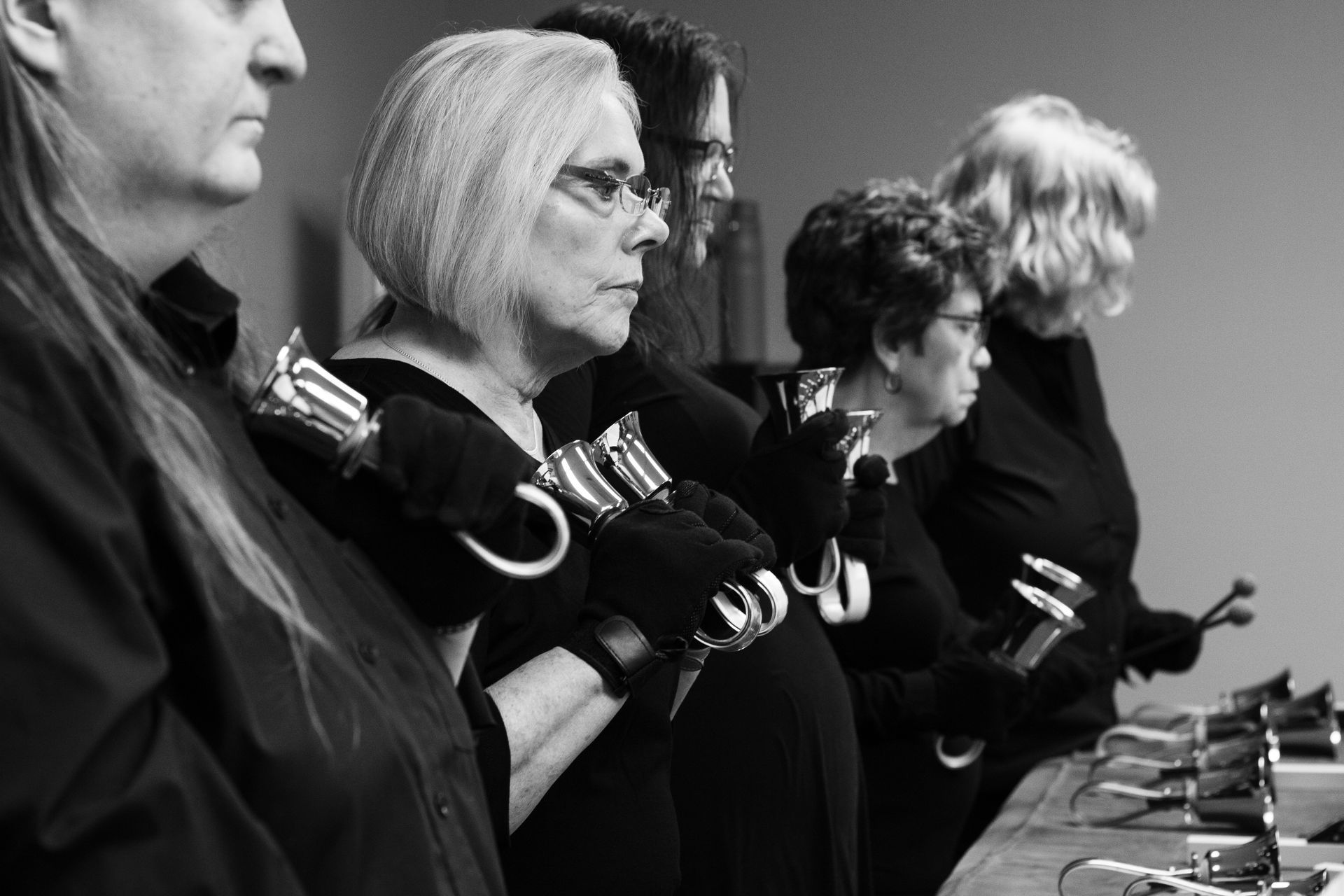 Handbell ensemble in black attire, playing bells. Black and white.
