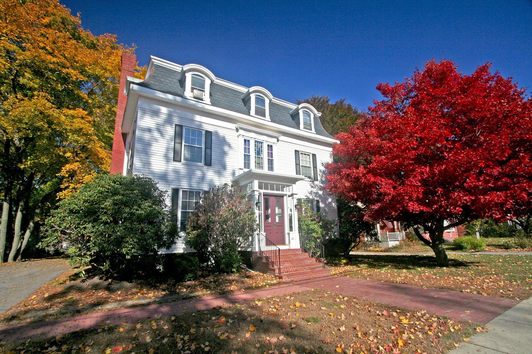 Exterior view of two story white home with red door  and trees in front yard.