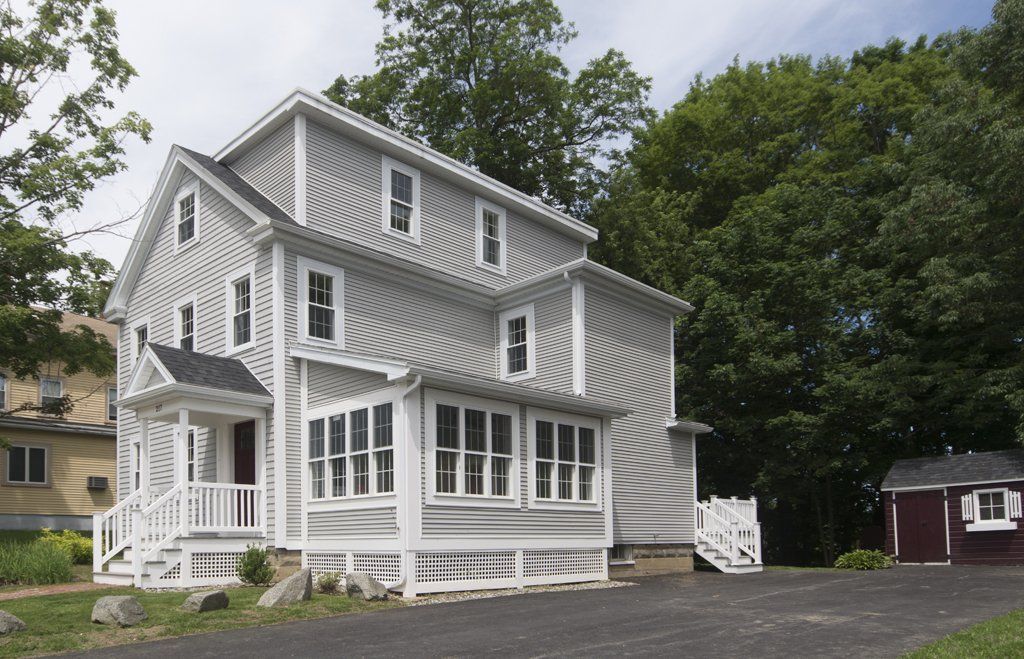 Exterior view of three story white home with chimney, covered patio, and large front yard with green grass.