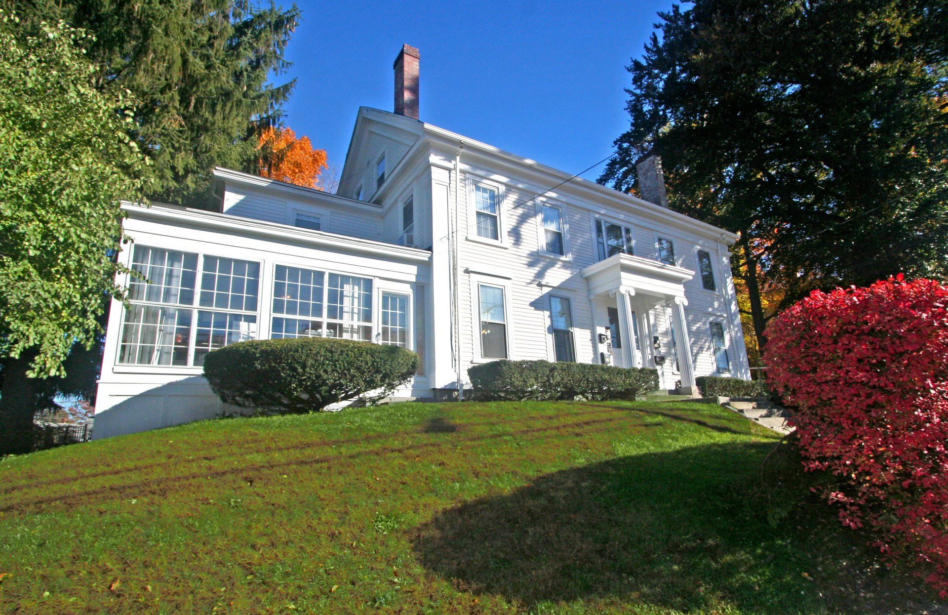 Exterior view of two story white home with chimney, covered patio, and large front yard with green grass.