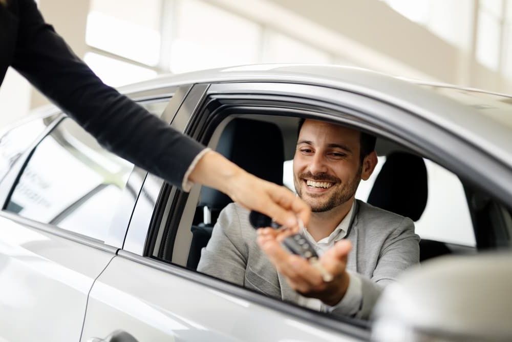 A Man Is Sitting in A Car Getting a Car Key from A Woman — Allan Ross Mechanical Repairs in Charmhaven, NSW