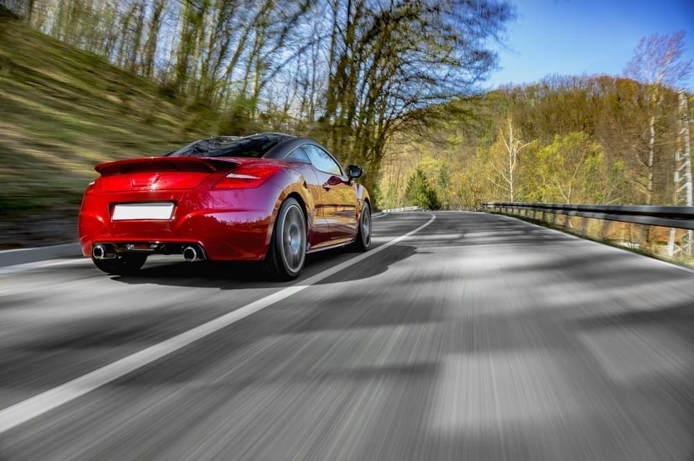 A Red Sports Car Is Driving Down a Country Road — Allan Ross Mechanical Repairs in Charmhaven, NSW