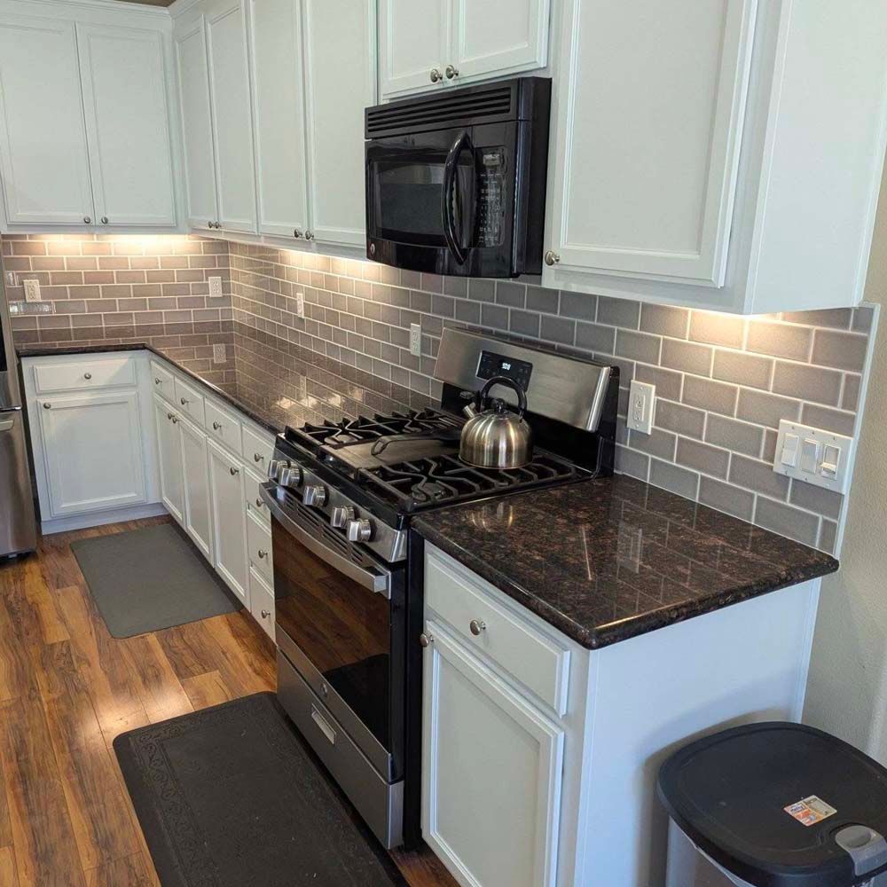 A kitchen with a stove , microwave , and a kettle on the counter.