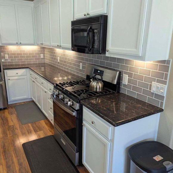 A kitchen with a stove , microwave , and a kettle on the counter.