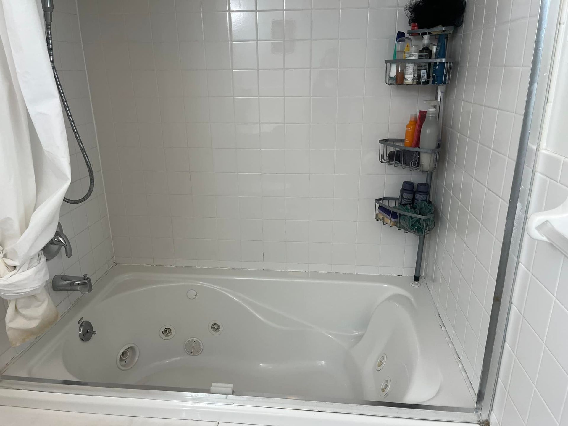 White bathtub with a shower curtain and shelving holding bath products.