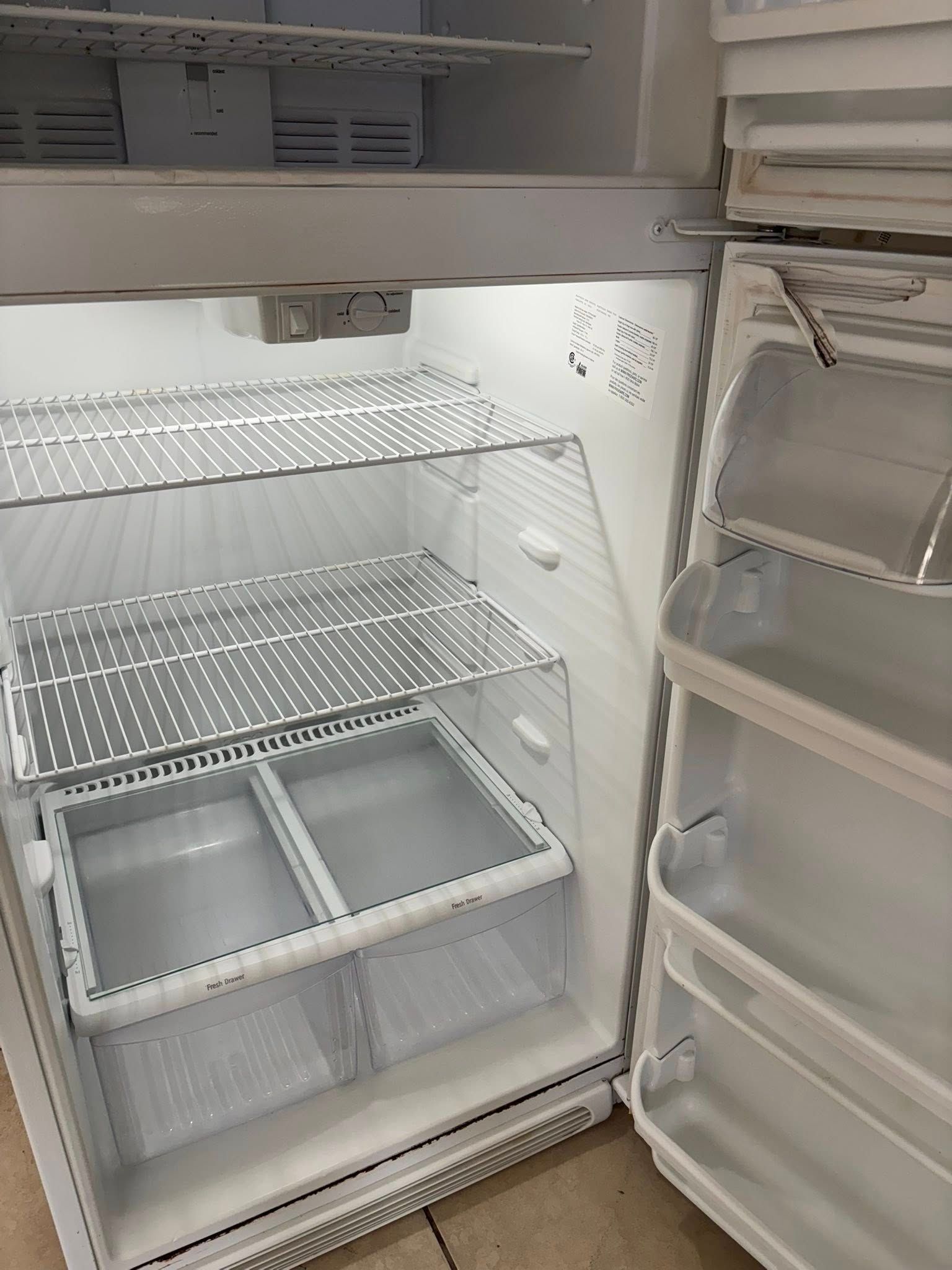 Empty white refrigerator interior with open door, showing shelves and storage bins.