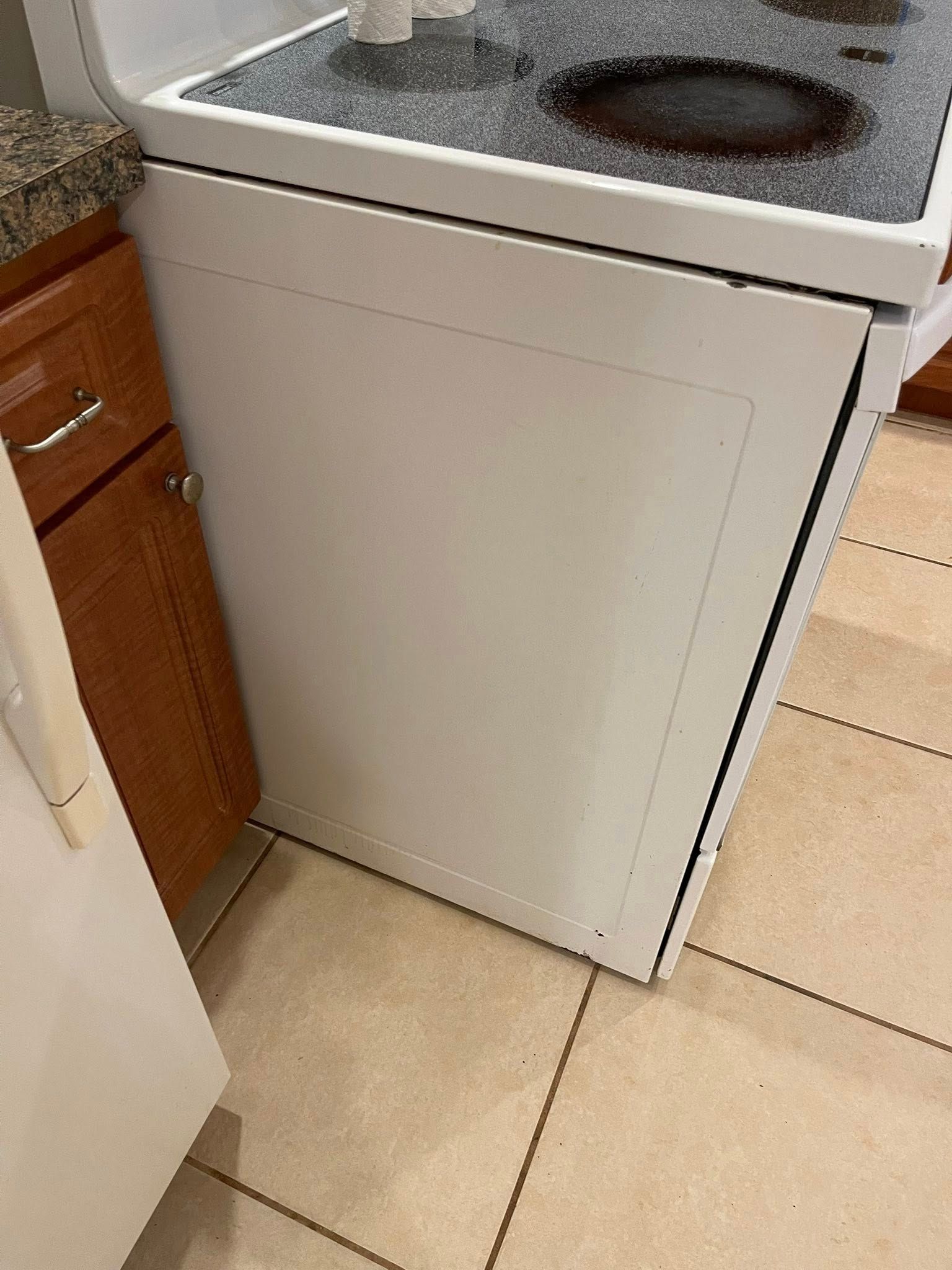 White oven side panel next to a brown cabinet and tile floor.