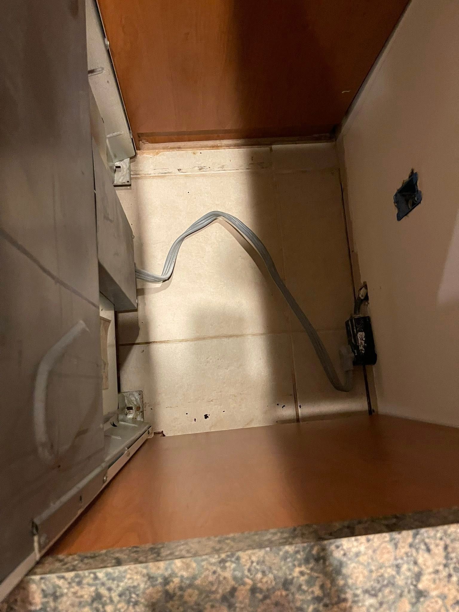 Inside of a kitchen cabinet with a coiled electrical cord, outlet, and cabinet drawer visible.
