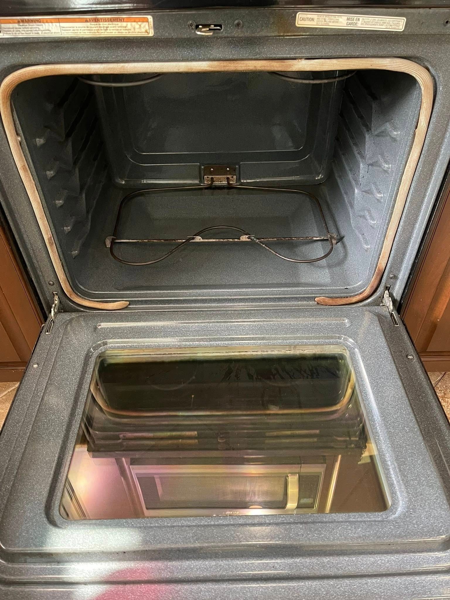 Open oven interior with a rack visible, black interior, glass door reflecting the room.