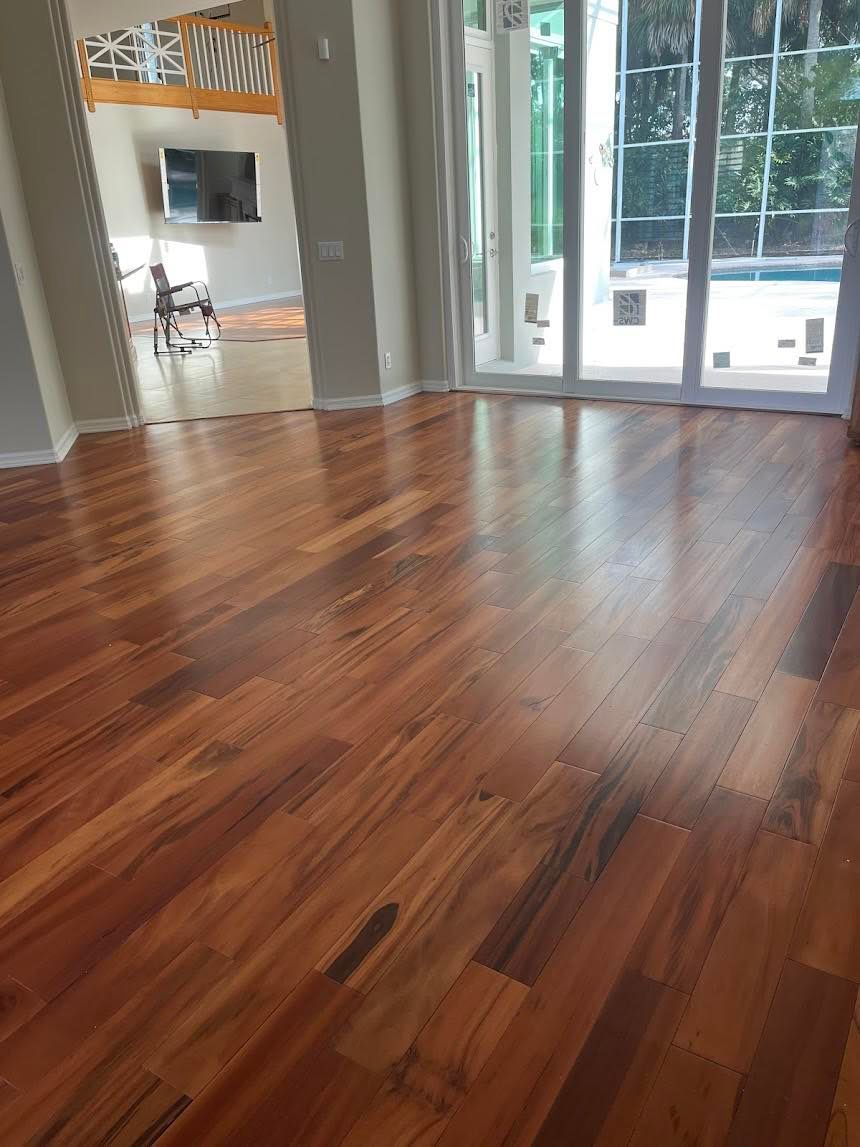 Polished hardwood floor in a home, reflecting sunlight from large windows overlooking a pool.