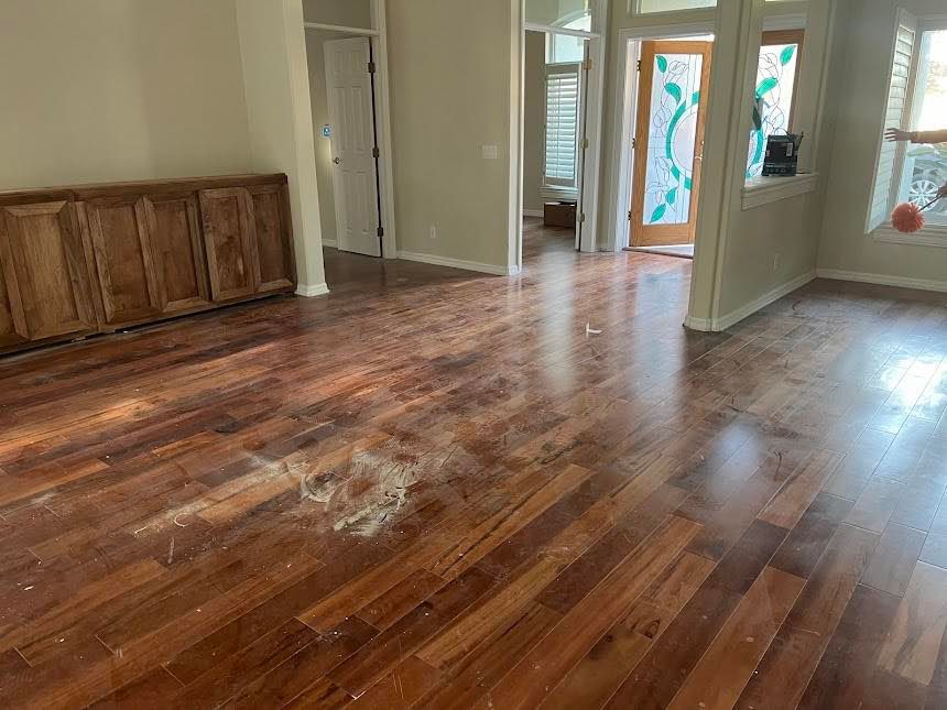 A room with wood flooring, debris, and built-in cabinets. An open doorway leads to another room.