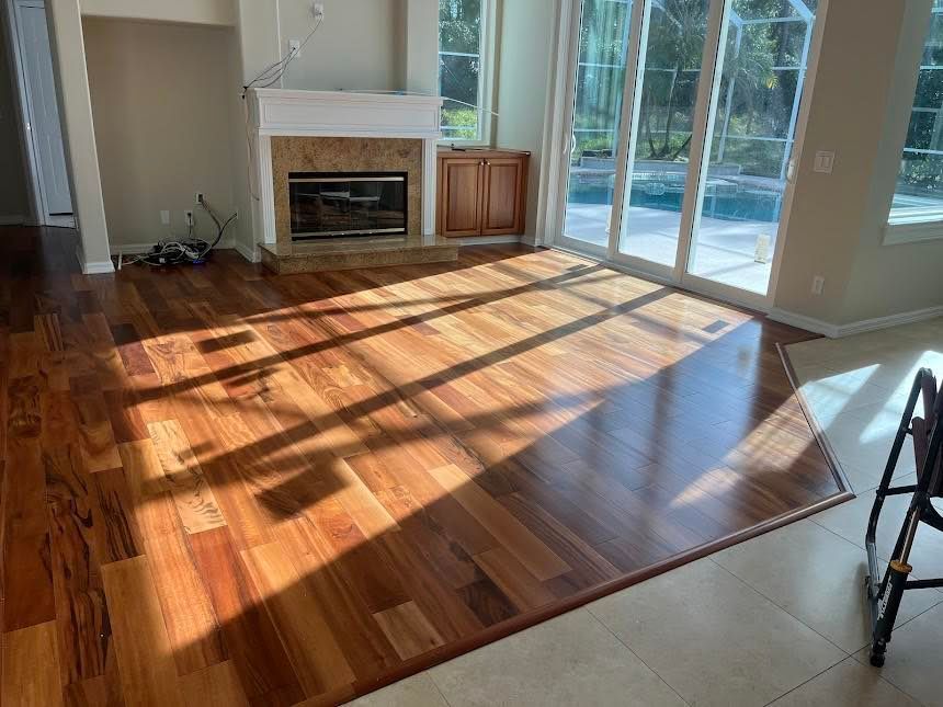 Wooden floor in a sunny room with a fireplace, sliding glass doors, and a tiled border.