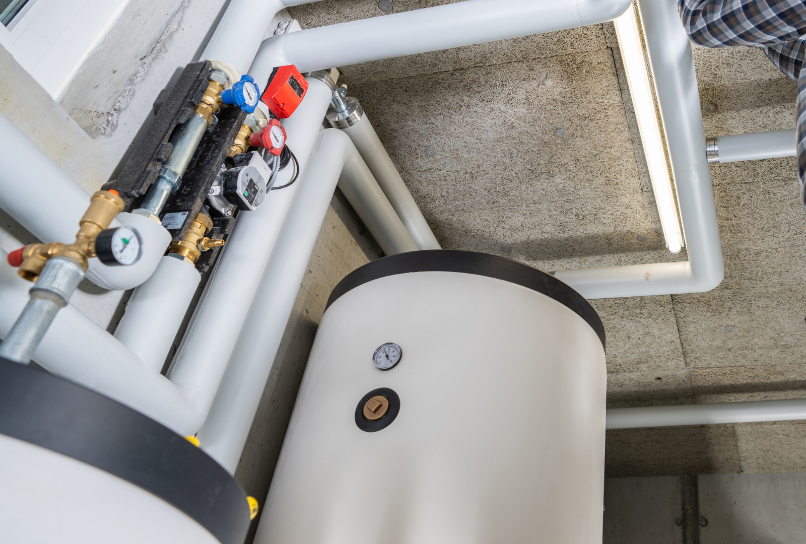 White water heater tank and piping system with pressure gauges and valves in a utility room.