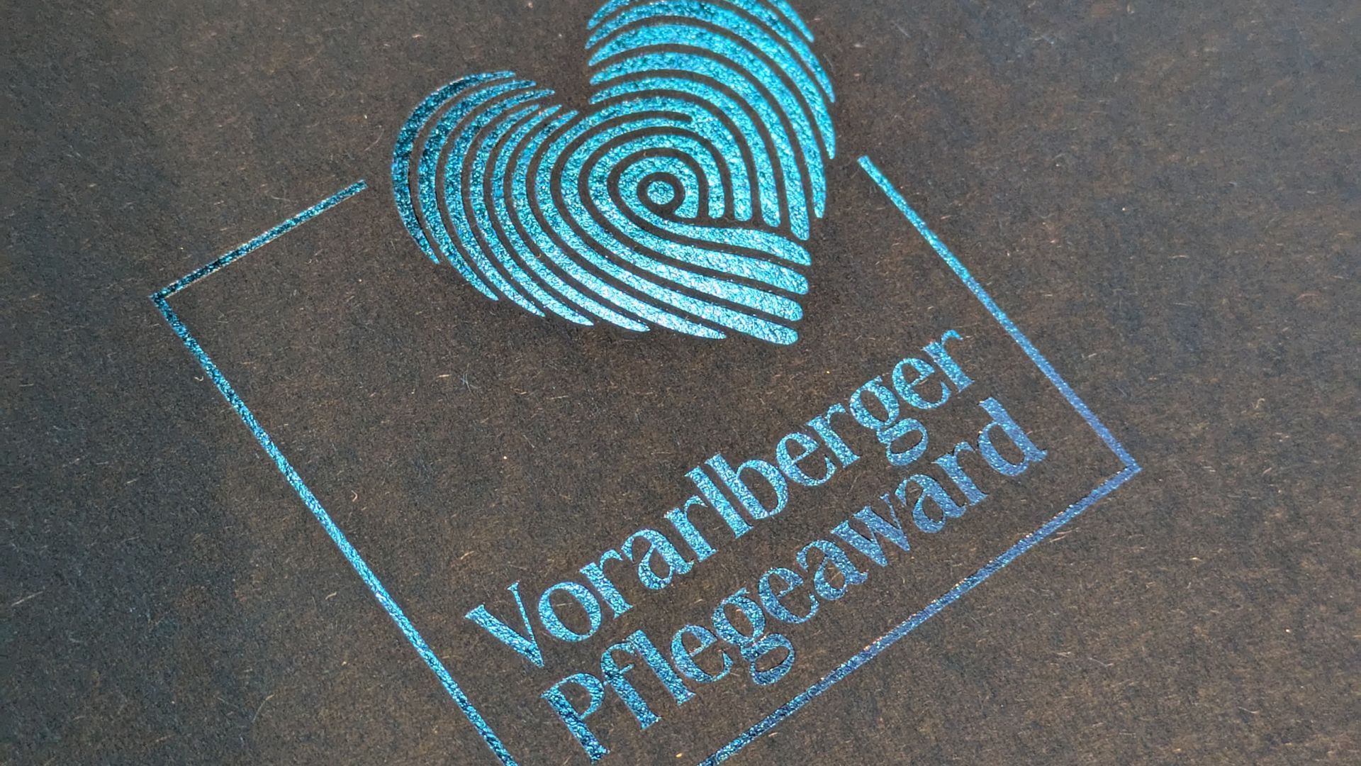 Das transparent aufgedruckte Logo strahlt durch türkisen Lichteinfall in den Farben des Pflegeawards auf der Urkundenmappe