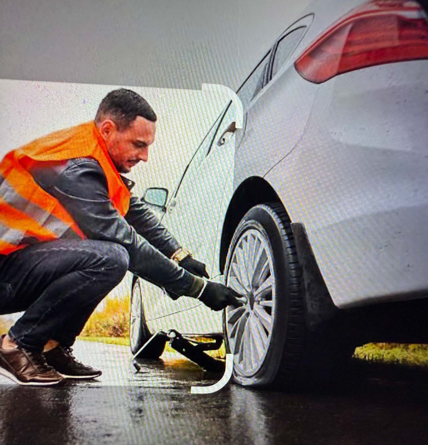 Person in orange vest changing a flat tire of a white car Person in orange vest changing a flat tire of a white car