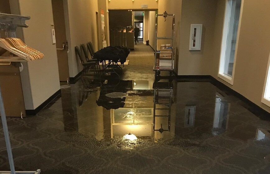 Flooded hallway with standing water reflecting lights and chairs along the walls