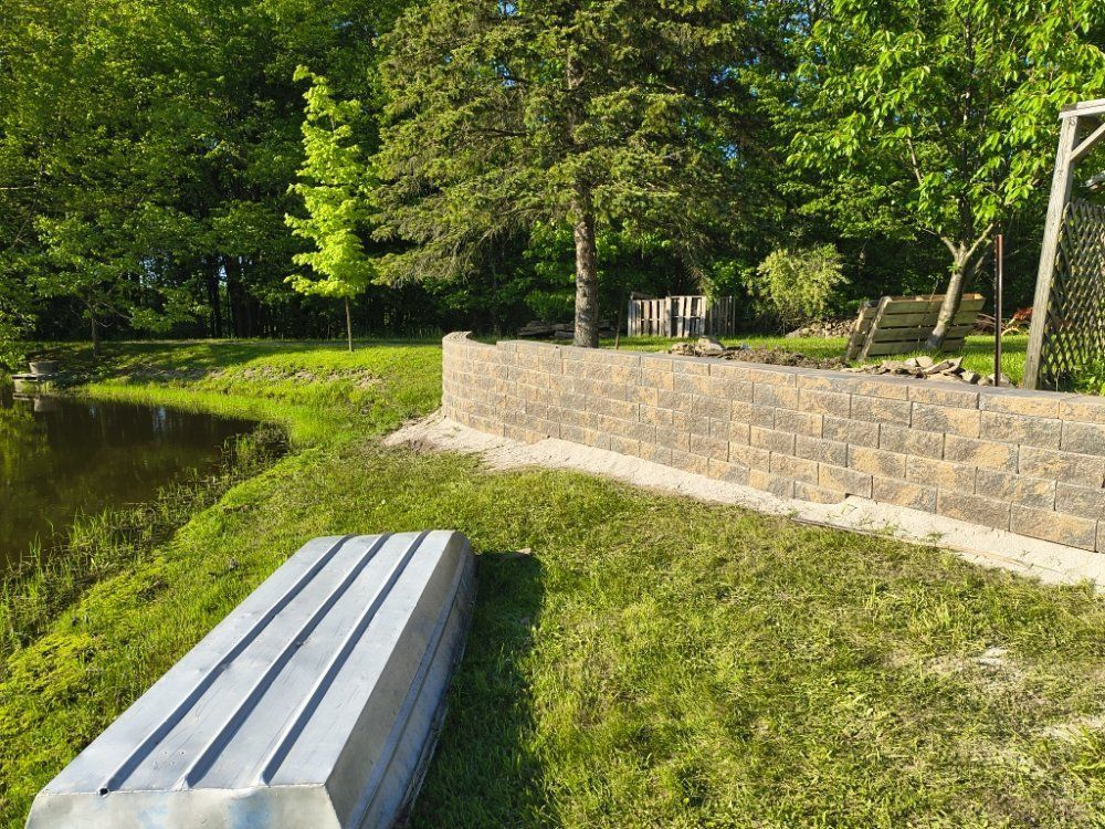 A concrete bench is sitting in the grass next to a brick wall.