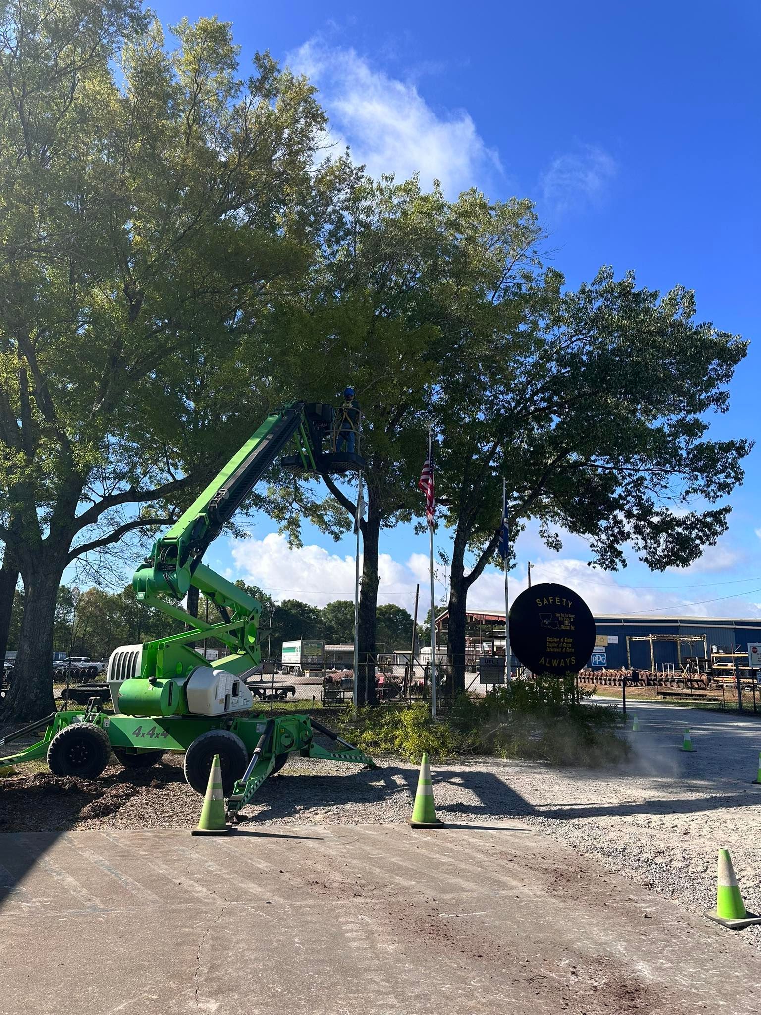 Green construction lift beside trees at a waterfront construction site with a large black pipe and gravel path