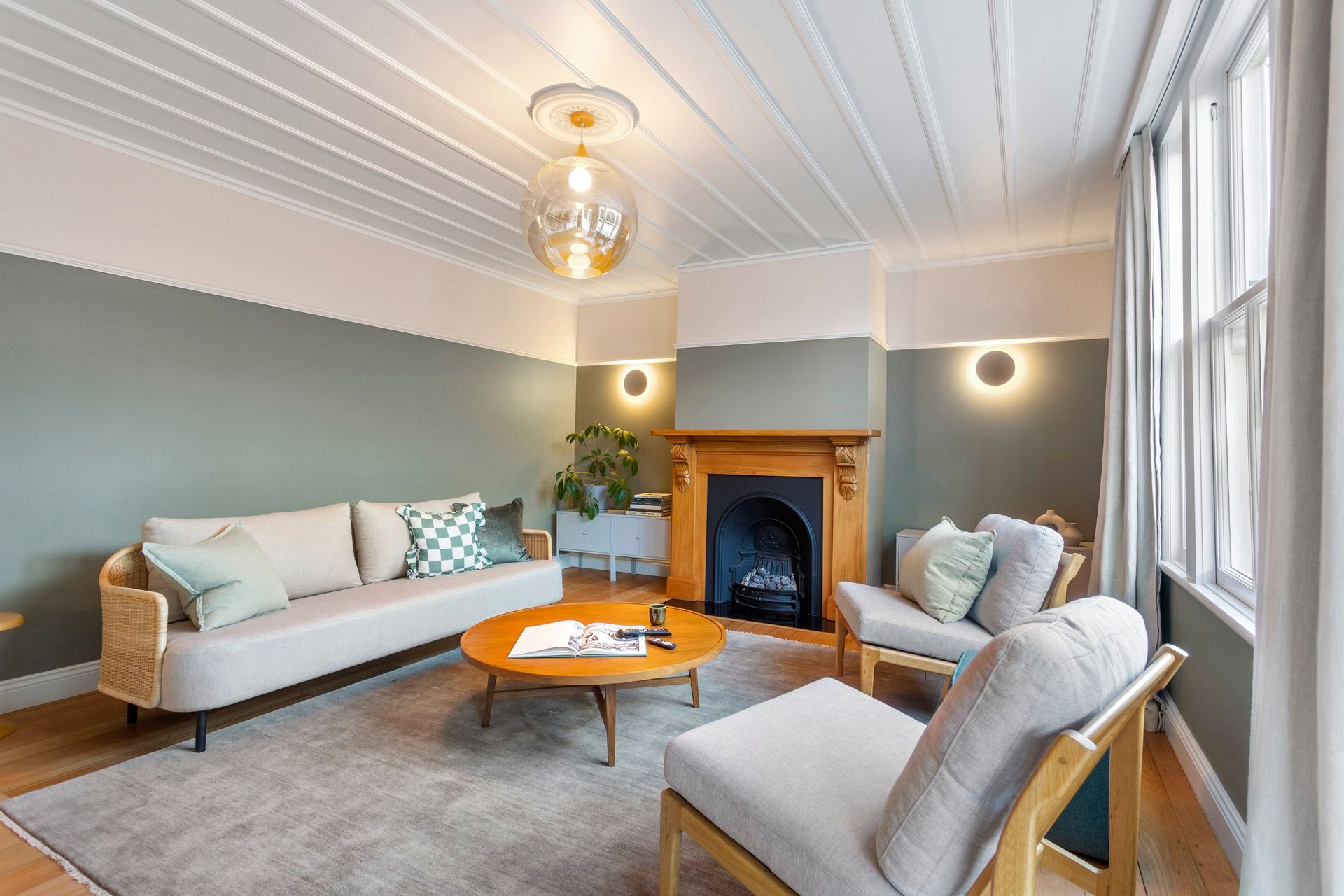 A cozy living room with a beige sofa, two armchairs, a wooden coffee table, and a fireplace with sage green walls.