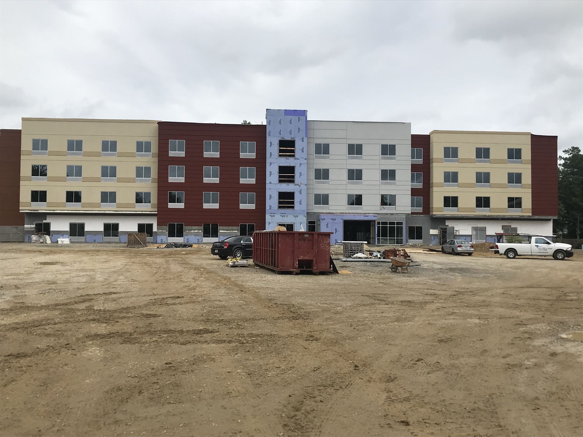 A large building under construction with a lot of cars parked in front of it.