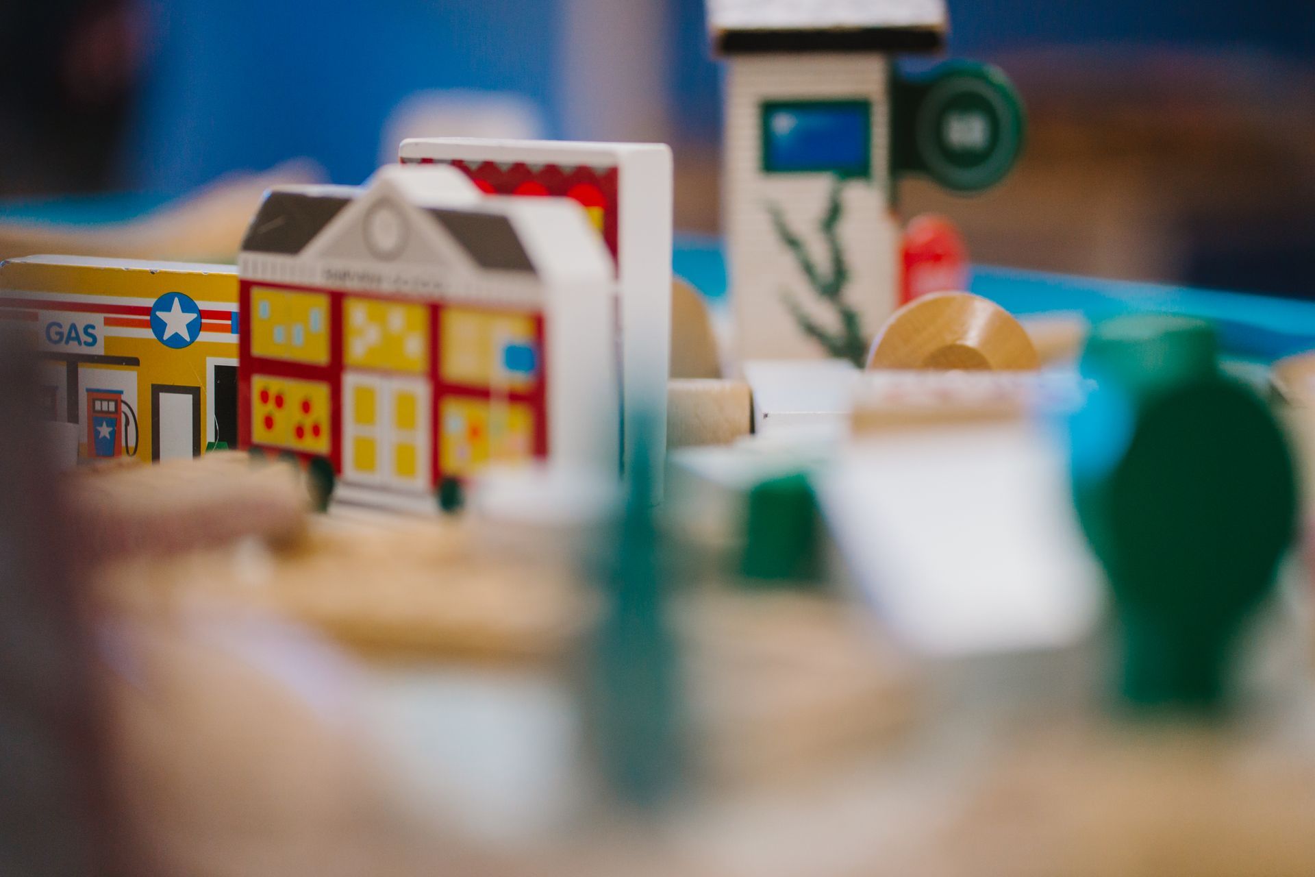 A wooden toy train set with a gas station in the background