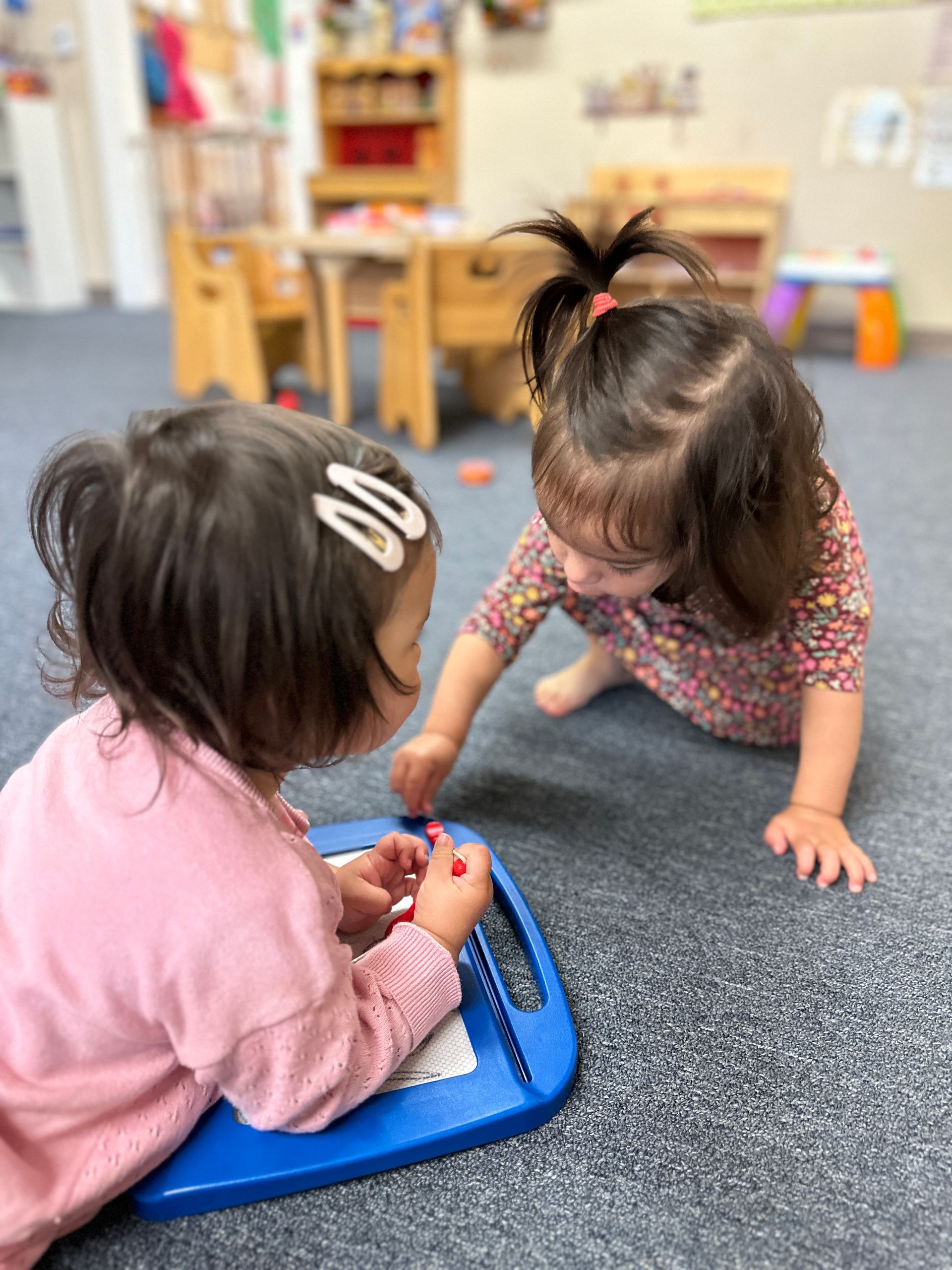 Two little girls are playing with a toy on the floor