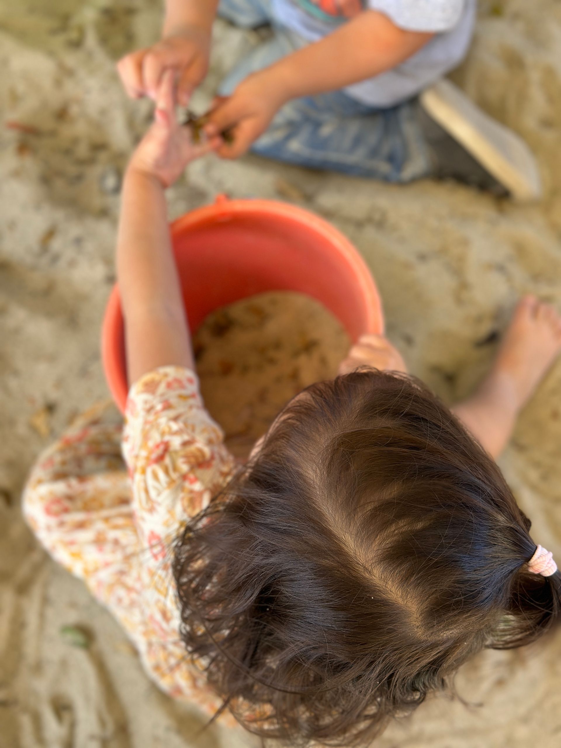 A little girl is playing in the sand with a red bucket