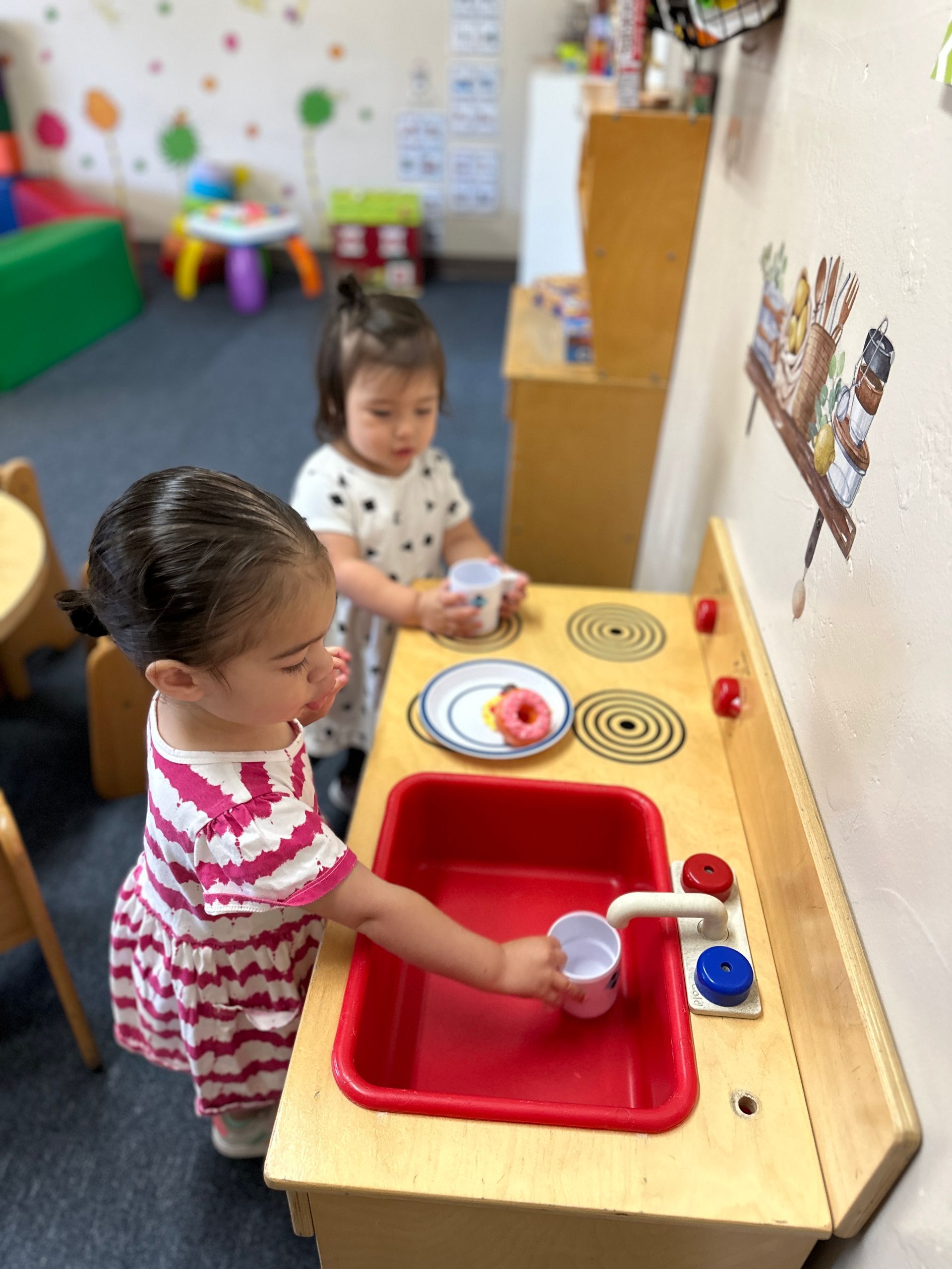 Two little girls are playing with a toy kitchen sink