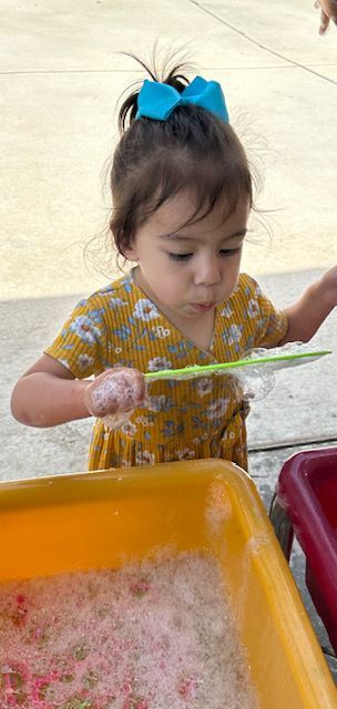 A little girl is playing with a spoon in a sensory bin.