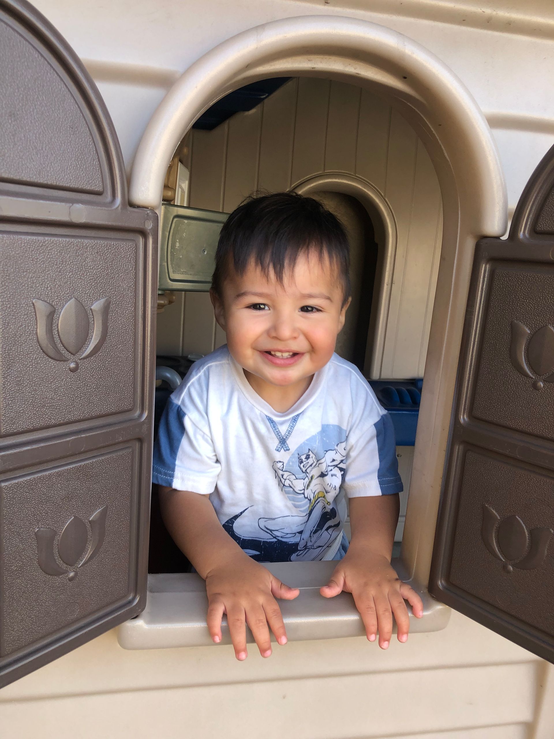 A little boy is playing in a playhouse and smiling