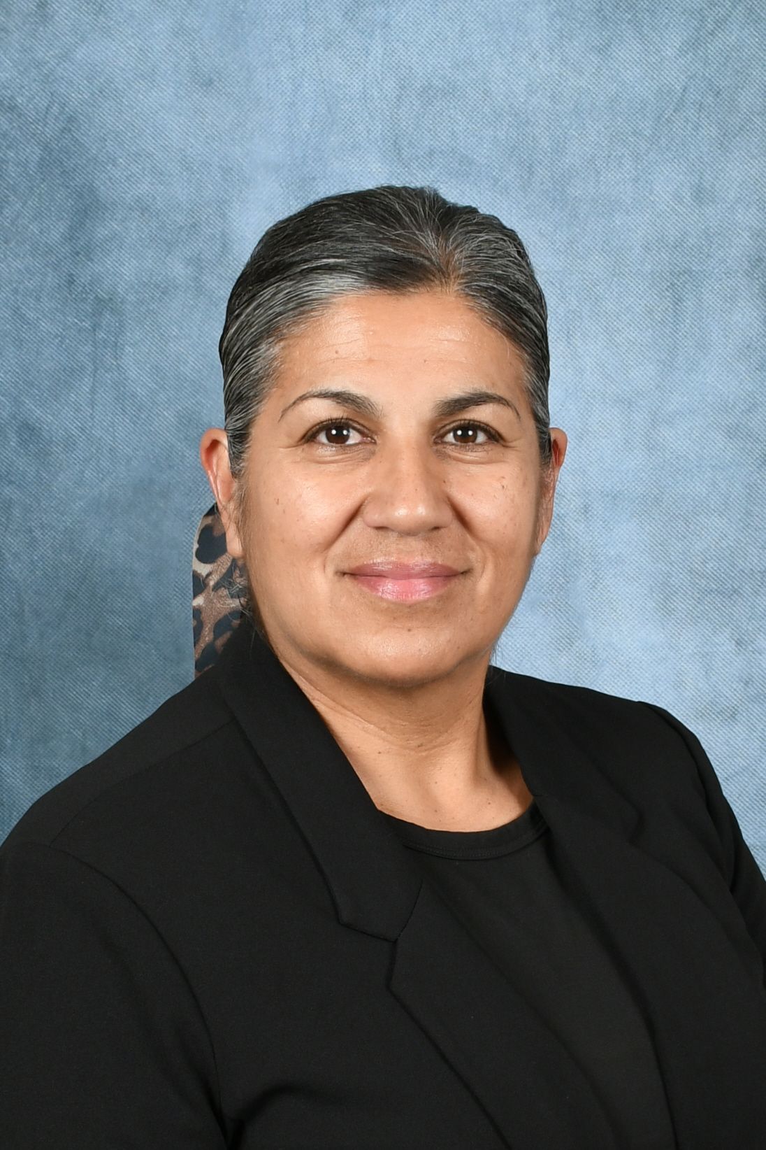 A woman wearing glasses and a floral shirt is standing in front of a tree.