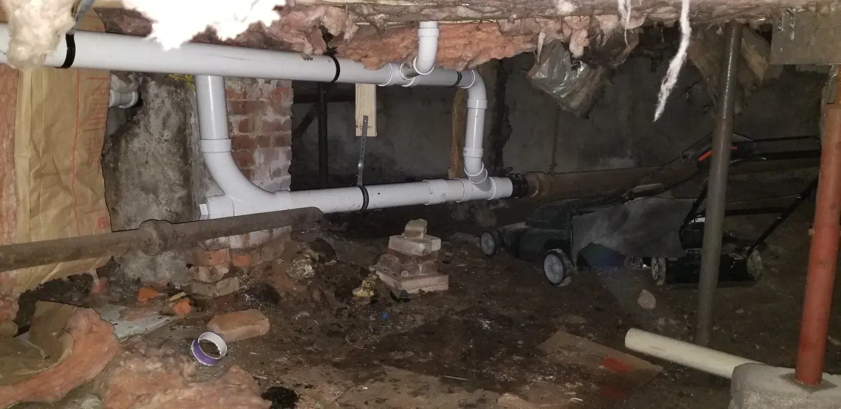 A basement with a lot of pipes and a brick wall.