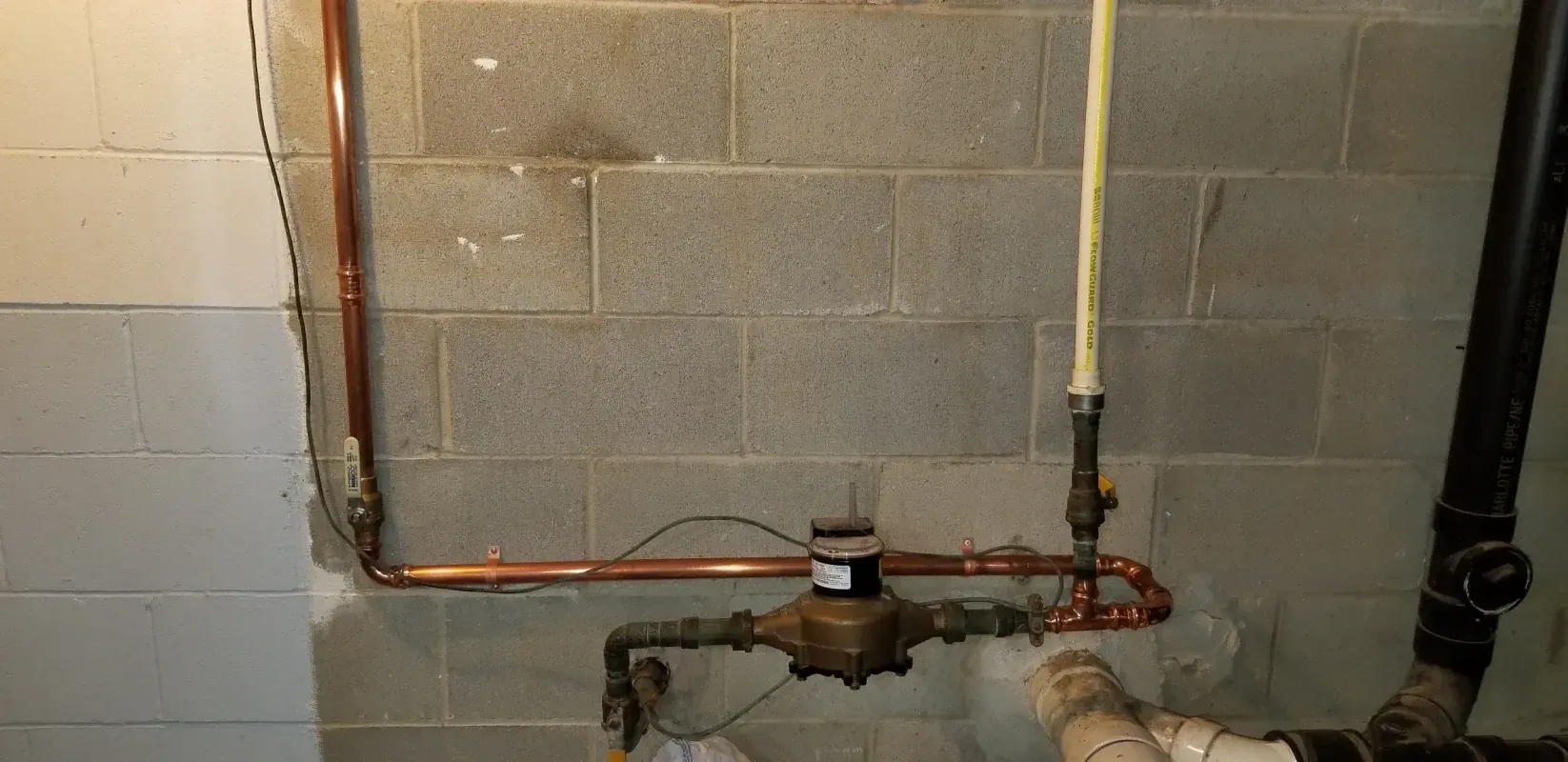 A water meter is attached to a copper pipe in a basement.