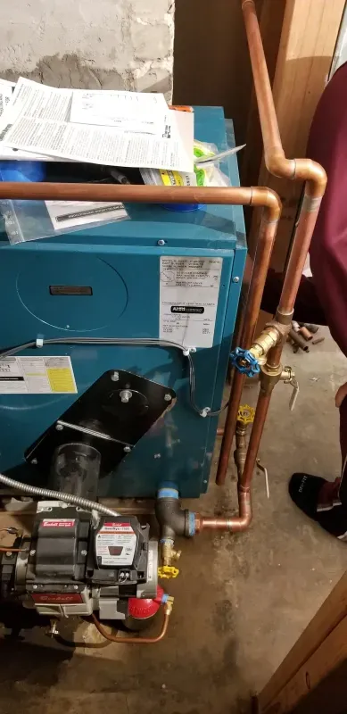 A blue boiler with copper pipes attached to it is sitting in a basement.