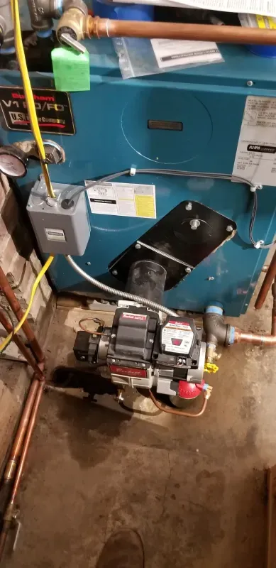 A blue boiler is sitting in a basement next to a brick wall.
