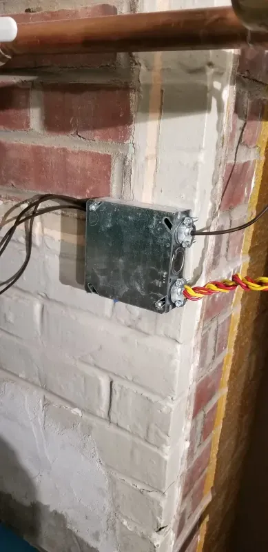A box with wires coming out of it is sitting on a brick wall.