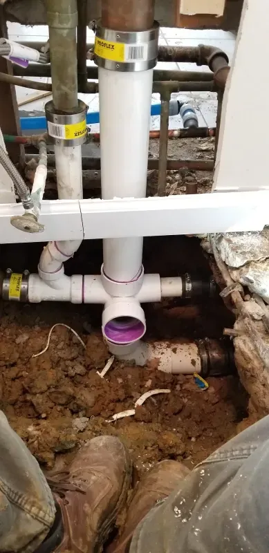 A plumber is working on a drain pipe in a basement.