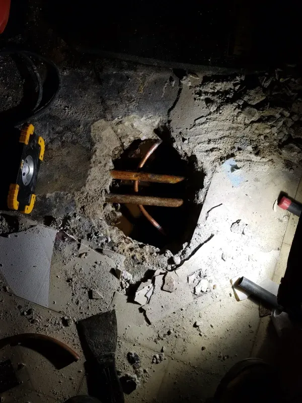 A person is looking into a hole in the ground with a flashlight.