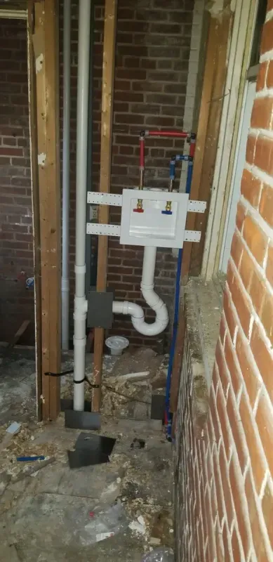 A drain pipe is being installed in a bathroom next to a brick wall.
