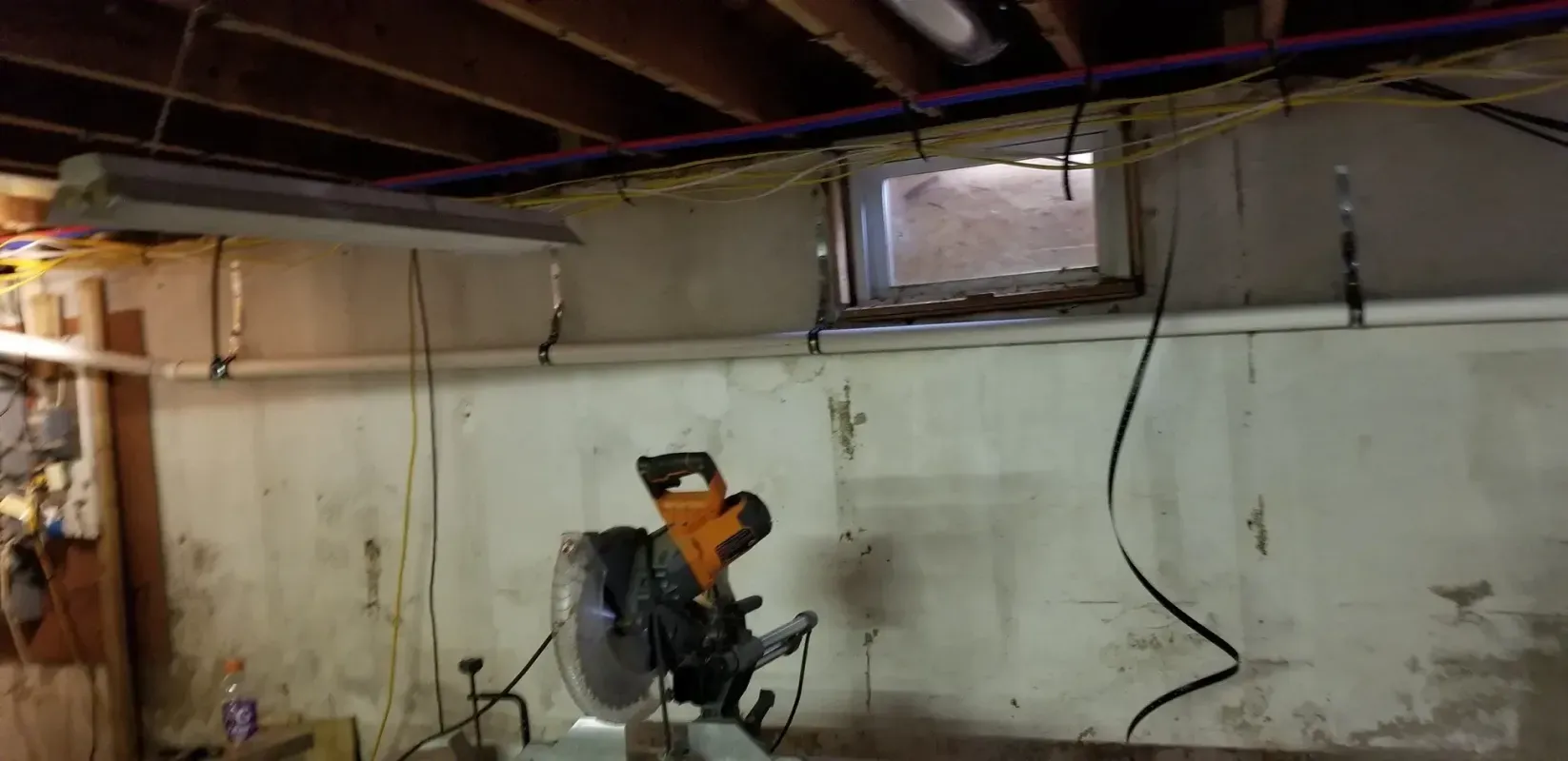 A circular saw is sitting in a basement next to a window.