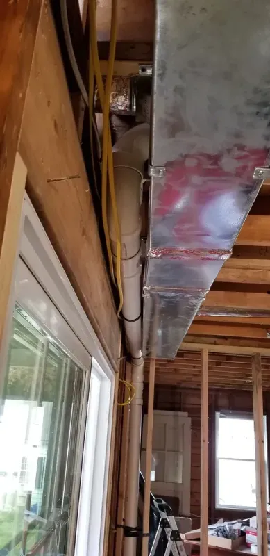 A large metal pipe is hanging from the ceiling of a house under construction.