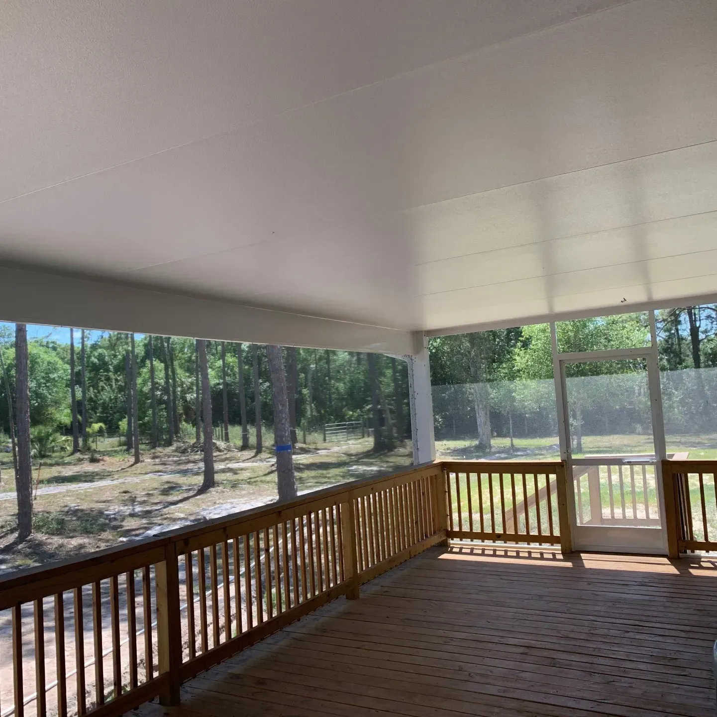 A screened in porch with a wooden railing and trees in the background.