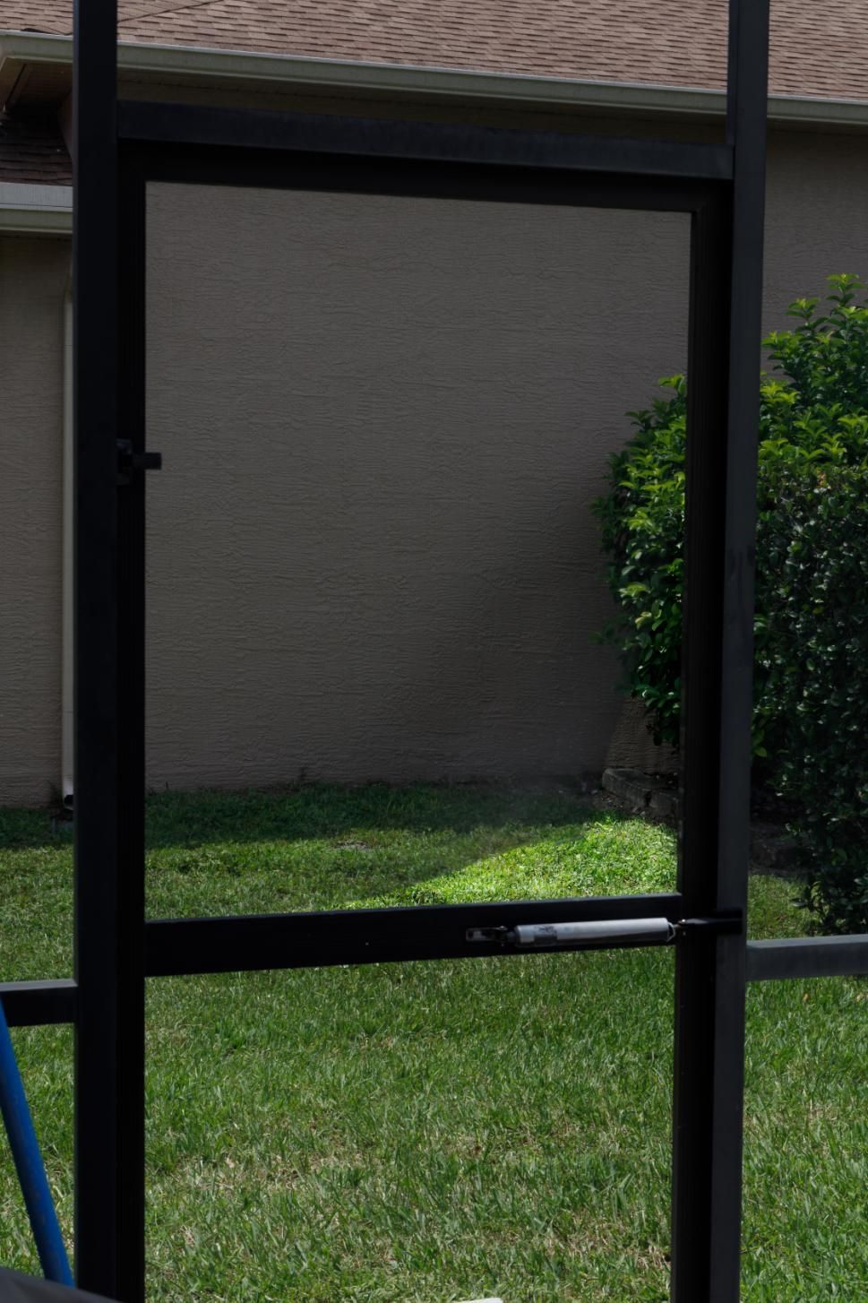 A screen door is sitting in the grass in front of a house.