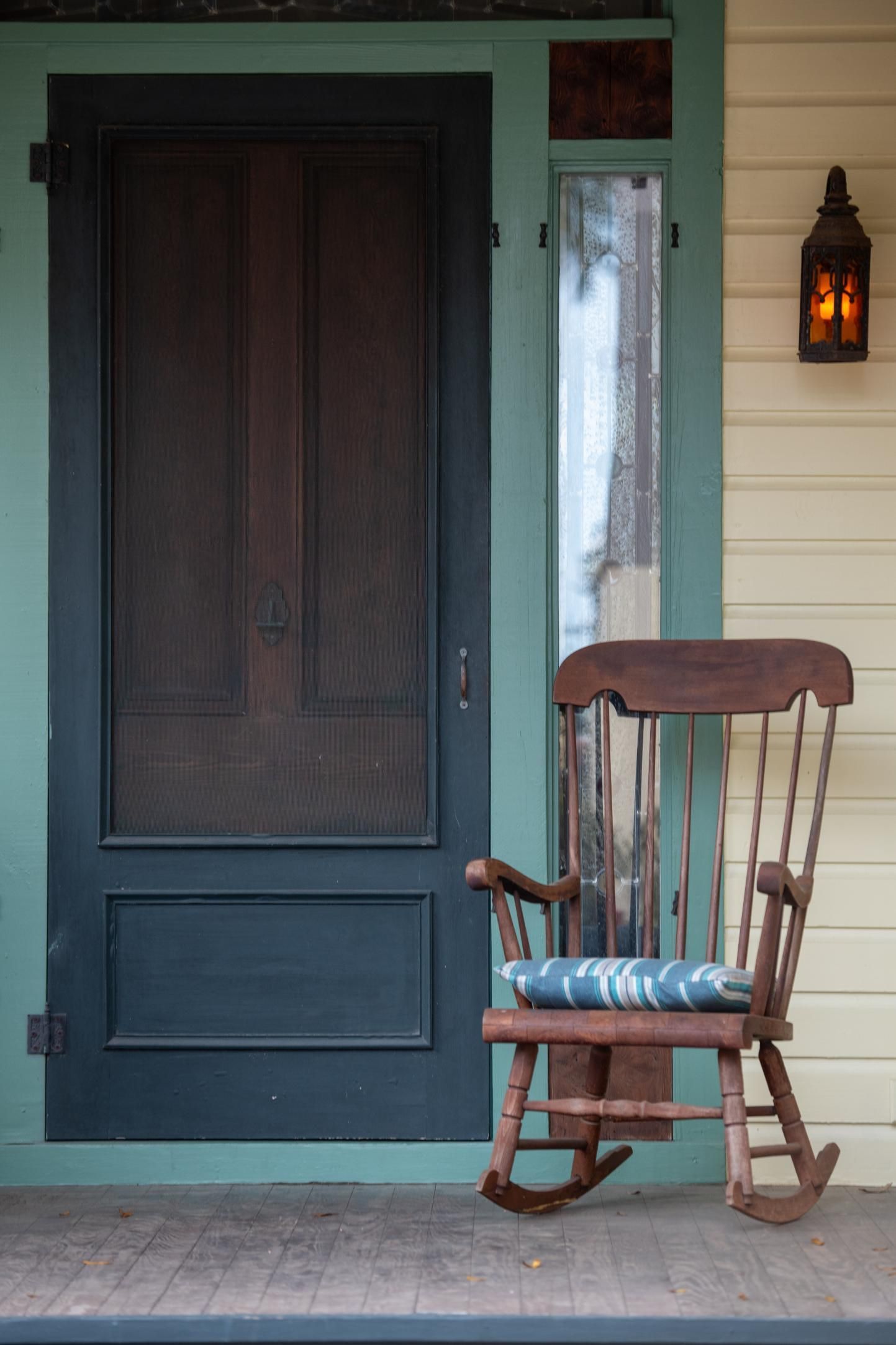 A rocking chair sits on a porch in front of a screen door.