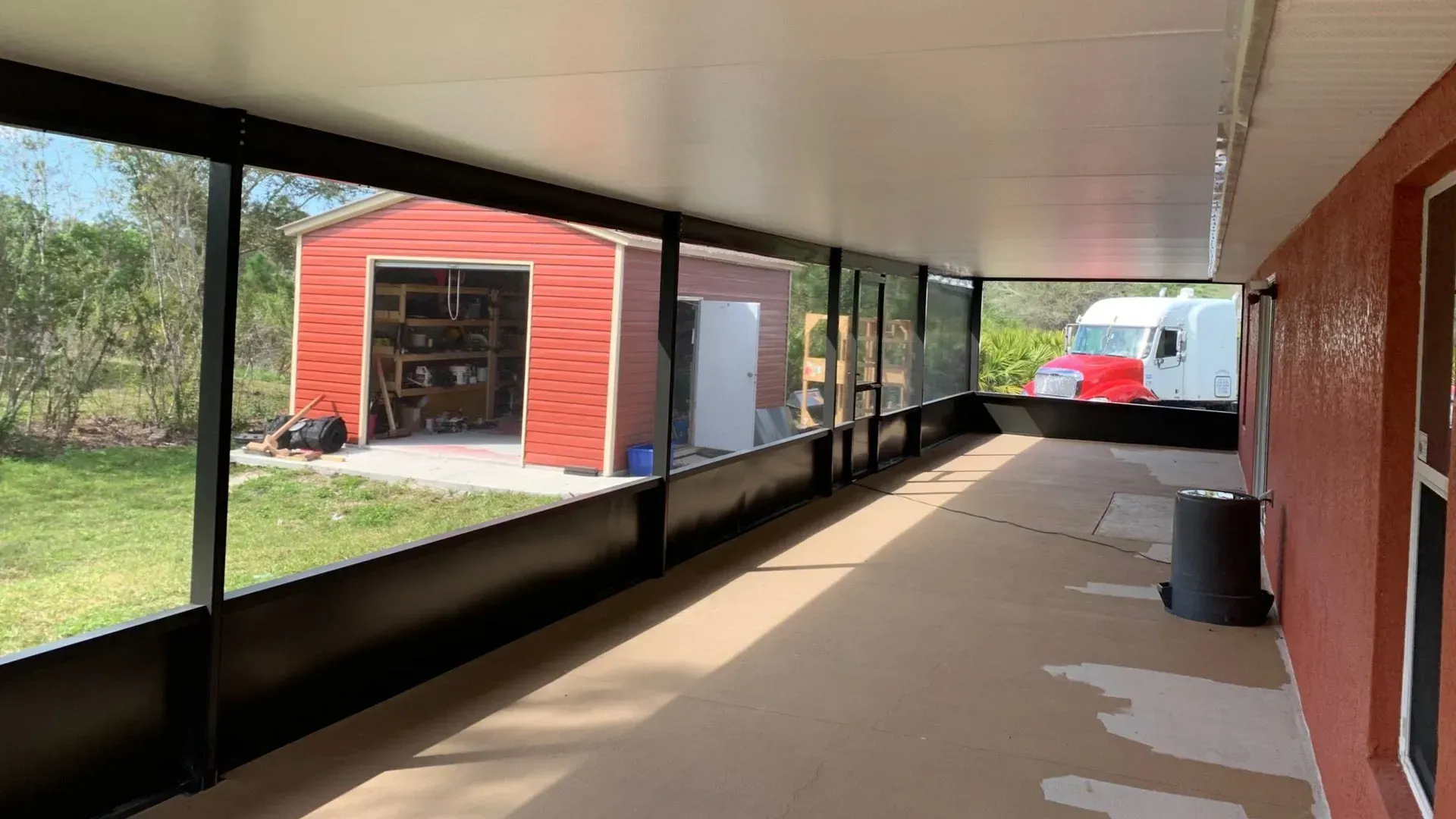 A large screened in porch with a red barn in the background.