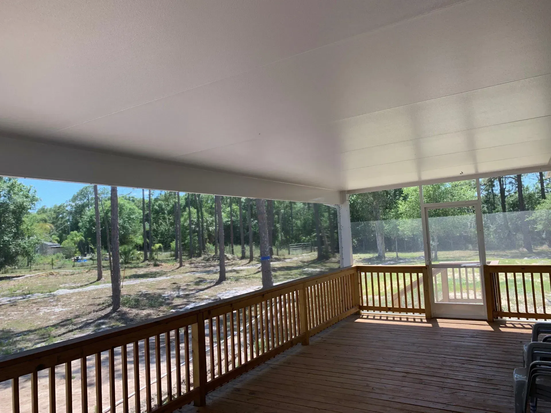 A screened in porch with a wooden railing and a view of a forest.