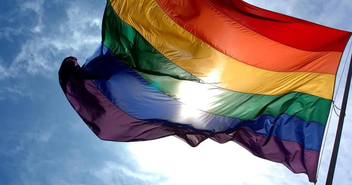 A rainbow flag is waving in the wind against a blue sky.