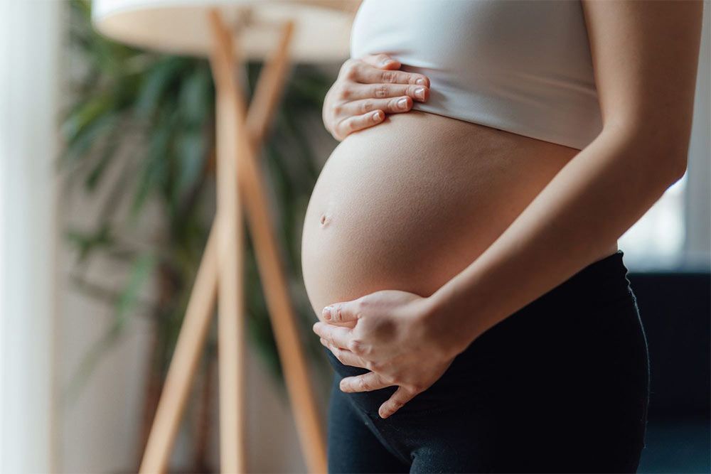 A pregnant woman is holding her belly in a living room.